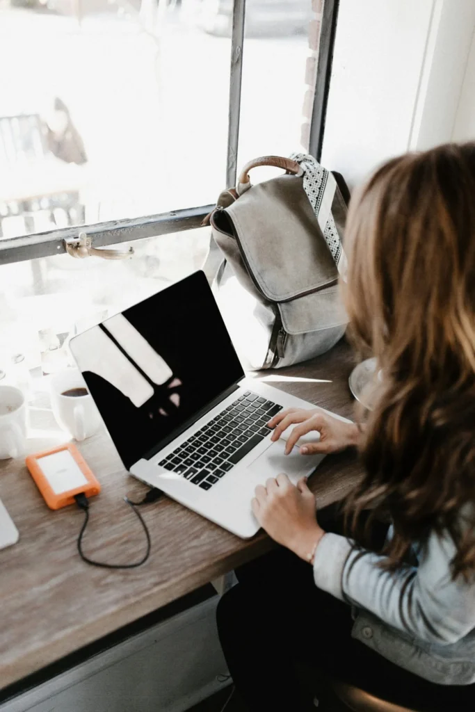 girl wearing grey long sleeved shirt using macbook pro on brown wooden table scaled 1